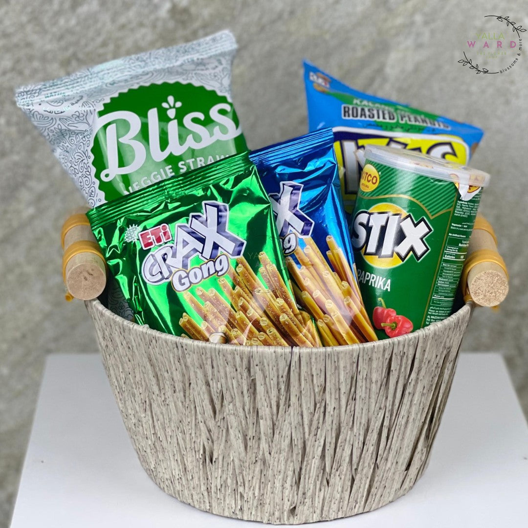 Basket filled with various snack packets including Bliss, Crax, and Stix on a neutral background.