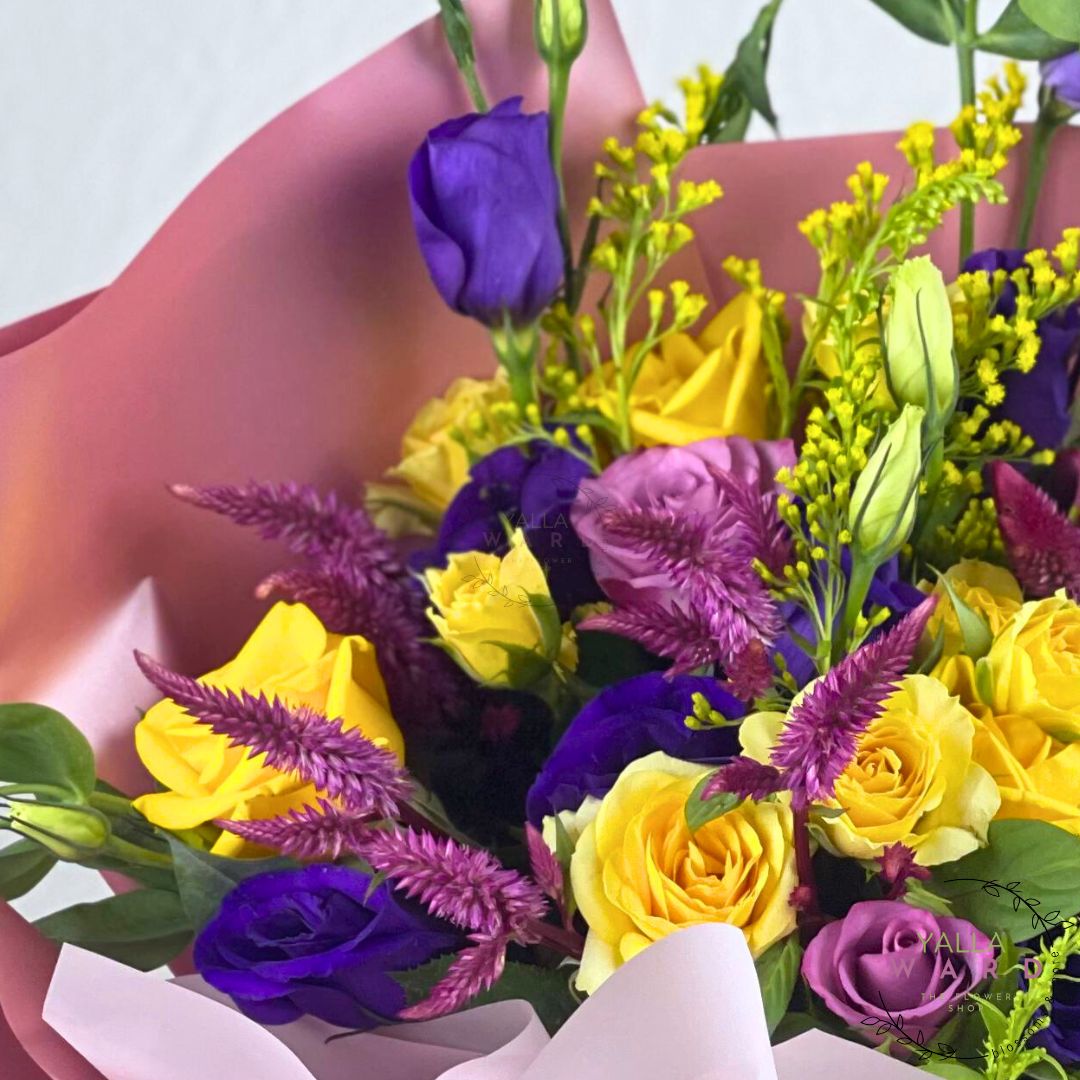 Bouquet of yellow and purple flowers held by a hand against a light background