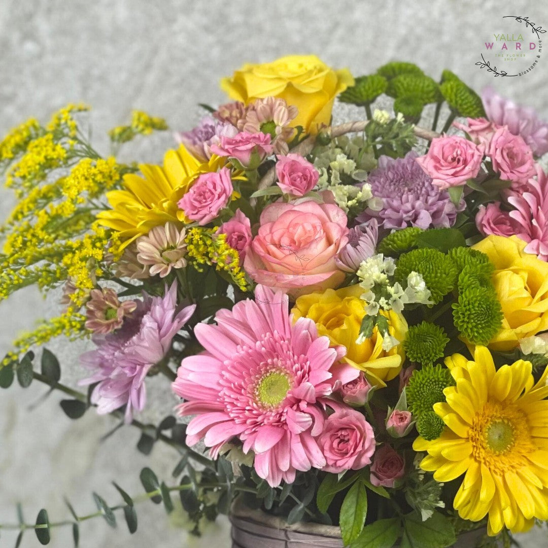 Bouquet of colorful flowers including pink, yellow, and green in a basket.