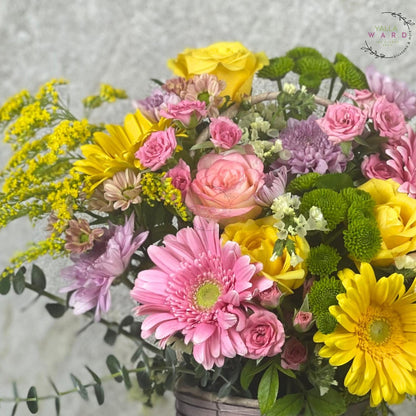 Bouquet of colorful flowers including pink, yellow, and green in a basket.