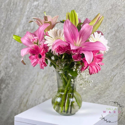 pink and white flowers in a clear vase on a textured surface with 'Yalla Ward' branding.