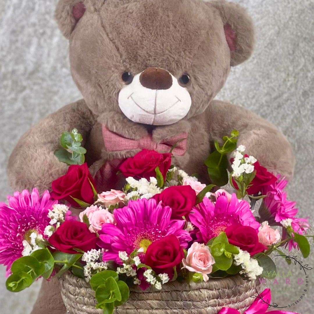 Teddy bear holding a basket of flowers against a neutral background