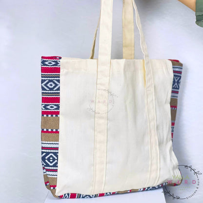 White tote bag with colorful patterned sides held by a person on a white background