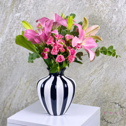 Striped vase with pink flowers on a white surface against a textured gray wall