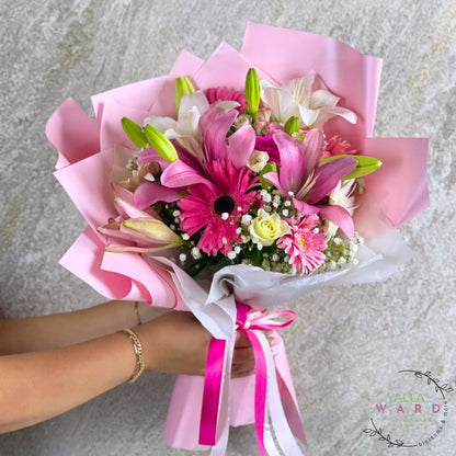 Bouquet of pink and white flowers with ribbons held by a person on a gray background