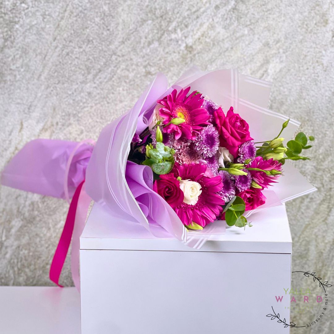 Bouquet of flowers wrapped in purple paper with a white box on a textured gray background