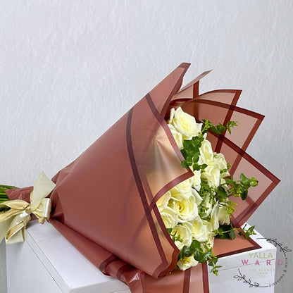 Bouquet of white roses wrapped in brown paper with a gold bow on a white surface.