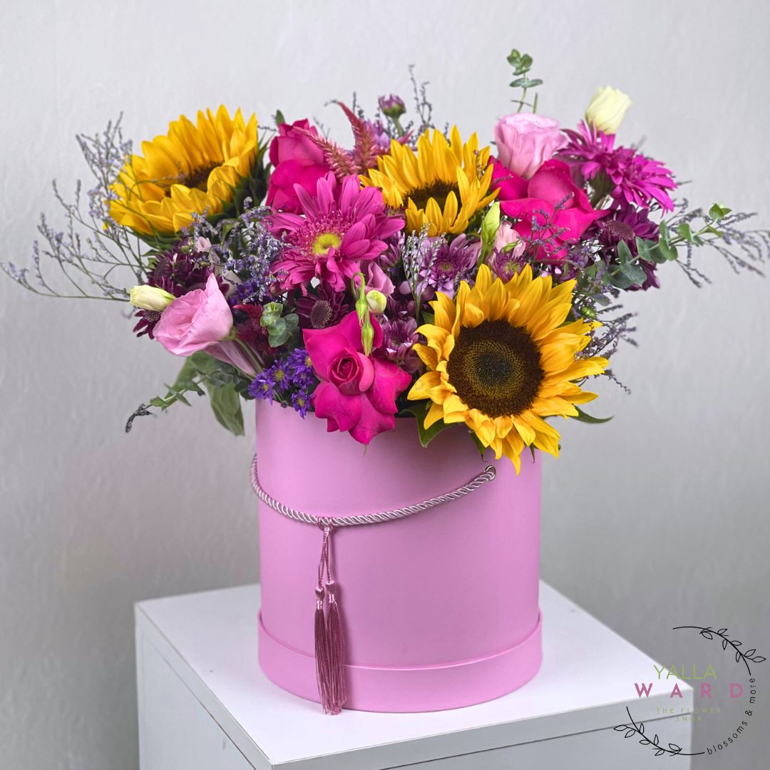 Colorful flowers and sunflowers in a pink box on a white surface with a light gray background