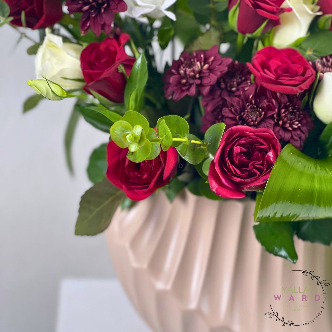 Bouquet of red and white flowers in a beige vase with a blurred background.