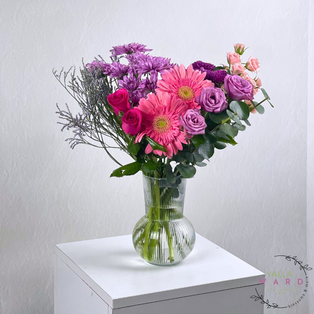 pink and purple flowers in a clear vase on a white surface with a light gray background.