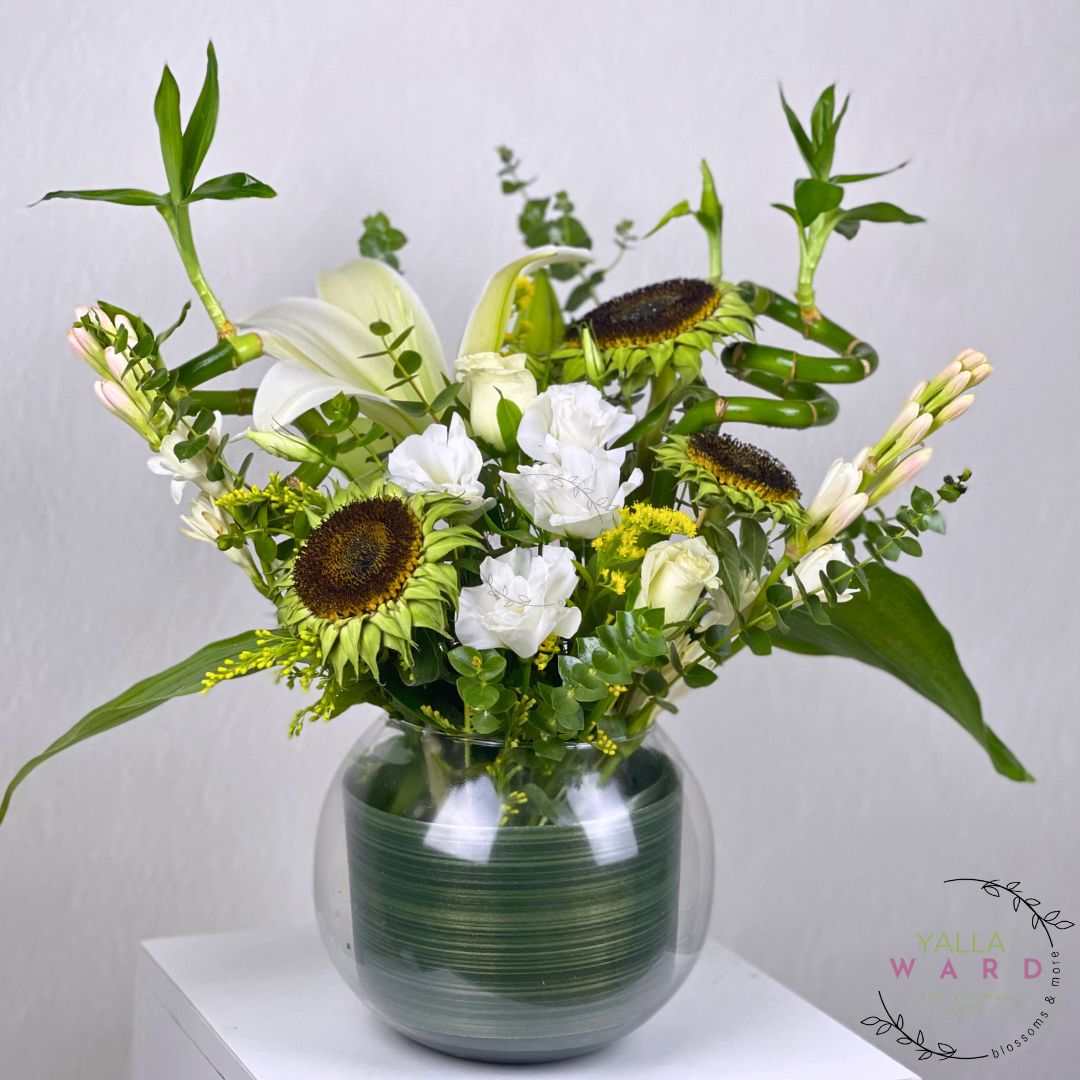 Bouquet of flowers in a green vase on a white surface with a light gray background