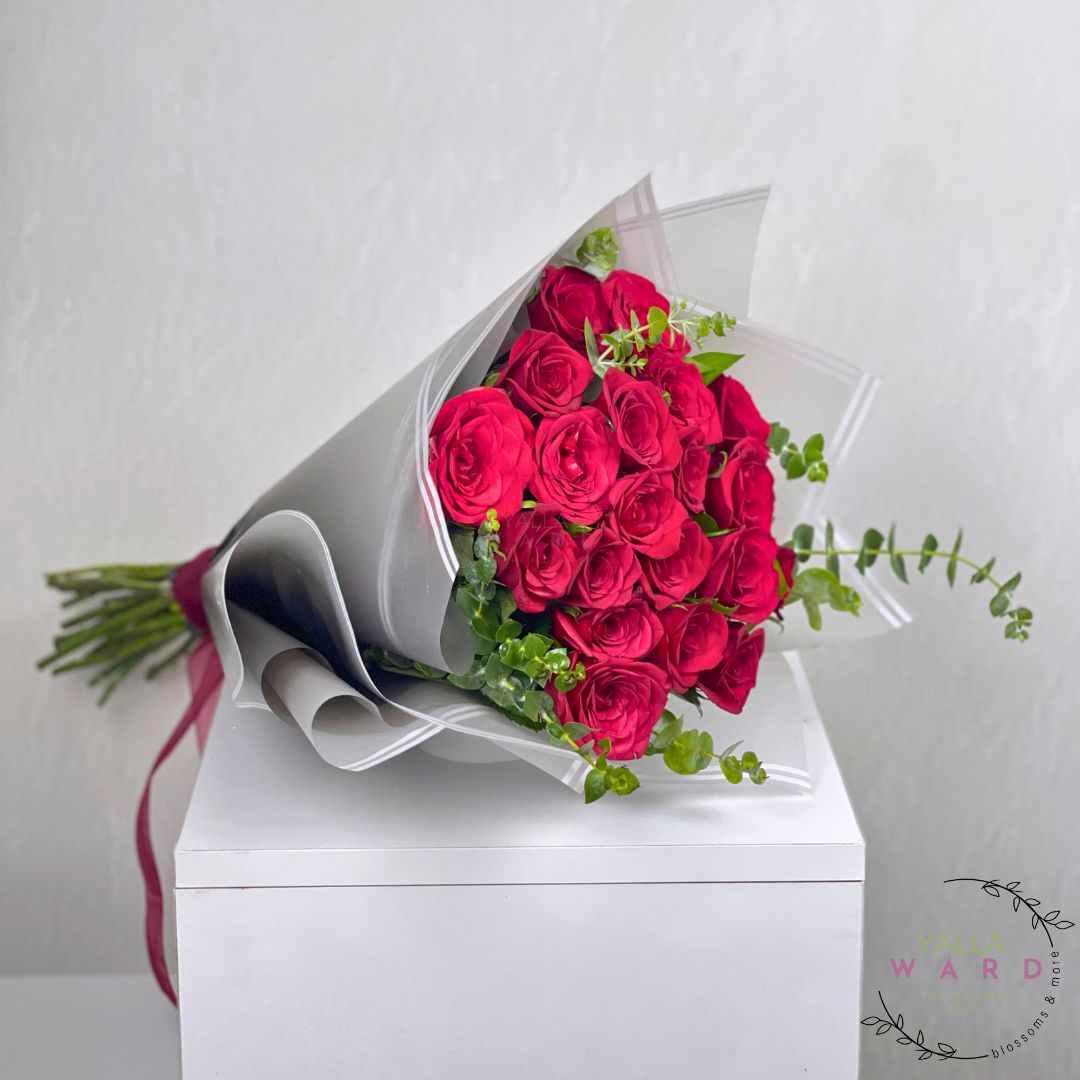 Bouquet of red roses wrapped in white paper on a white surface with a light gray background.