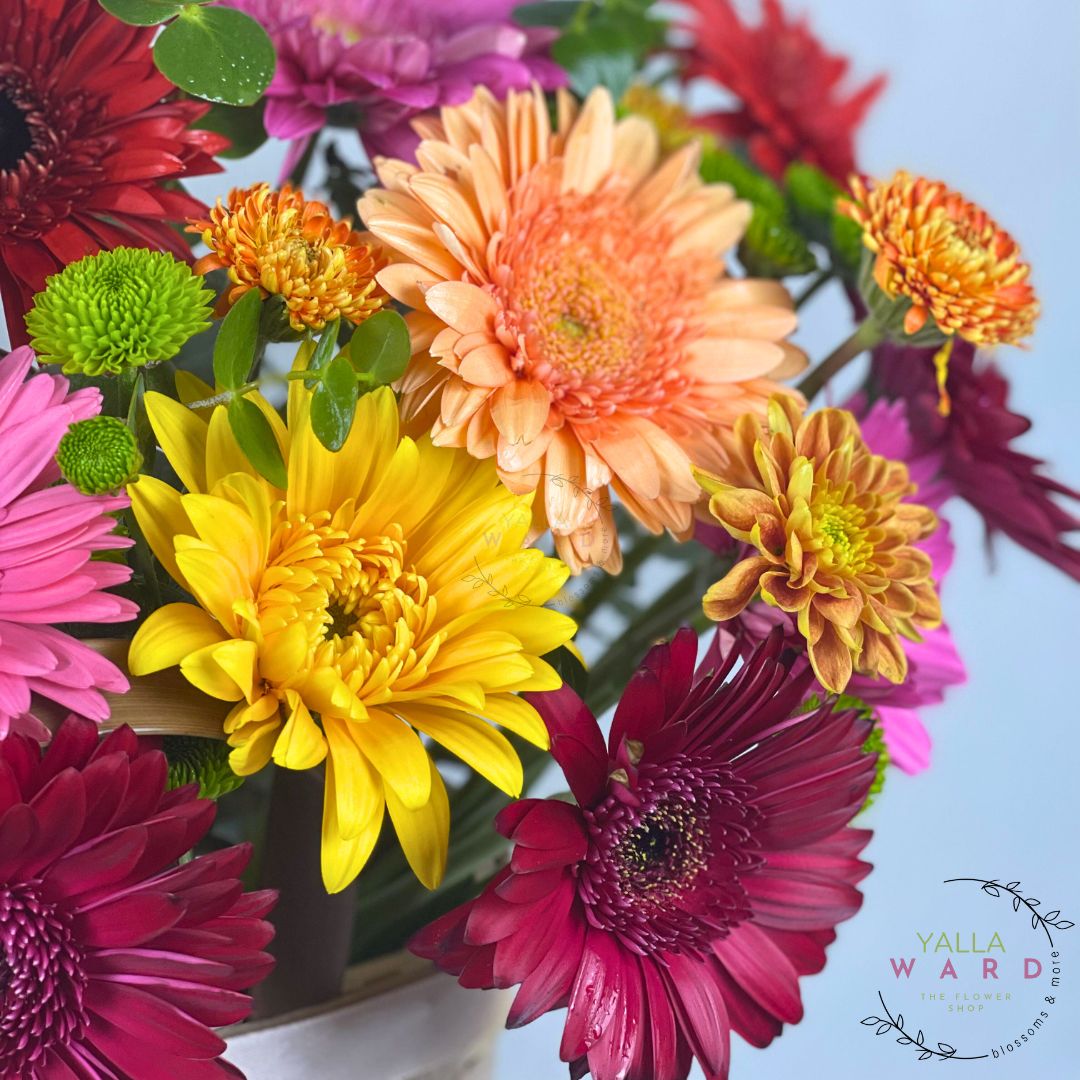 Bouquet of colorful flowers including yellow, pink, orange, and red in a white vase.