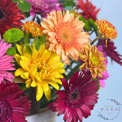 Bouquet of colorful flowers including yellow, pink, orange, and red in a white vase.