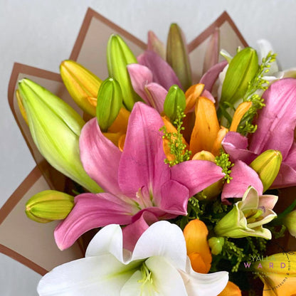 Bouquet of colorful Lilles including pink, white, and orange lilies on a light background.
