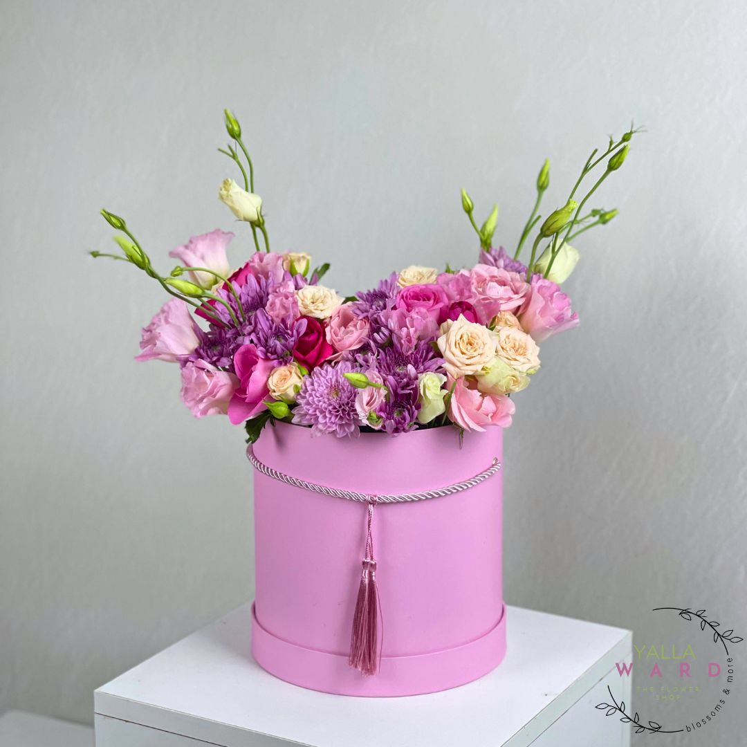 Pink flower box with a bouquet of flowers on a white surface against a gray background
