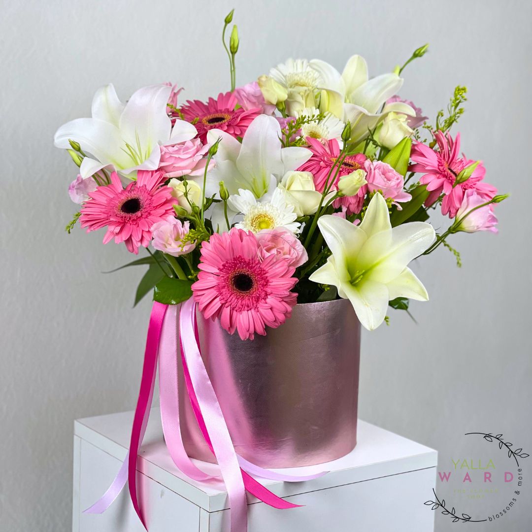 pink and white flowers with ribbons in a metallic pot on a white surface.