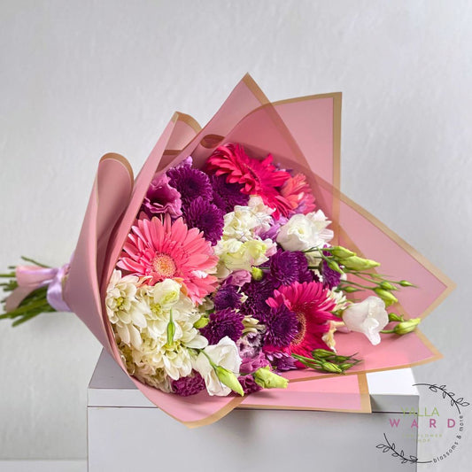 Bouquet of pink flowers wrapped in pink paper on a white surface