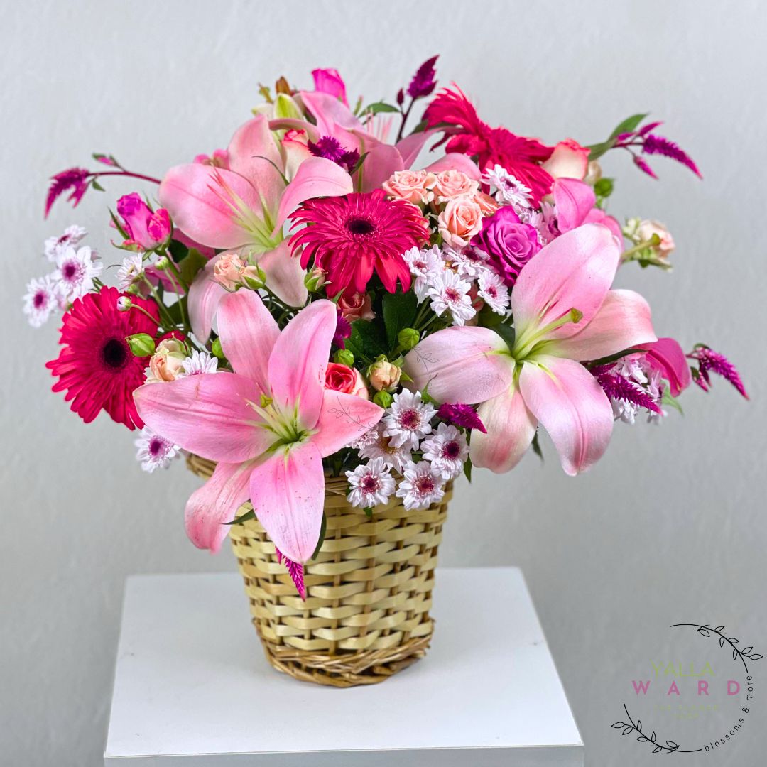 pink flowers in a woven basket on a white surface with a light gray background.