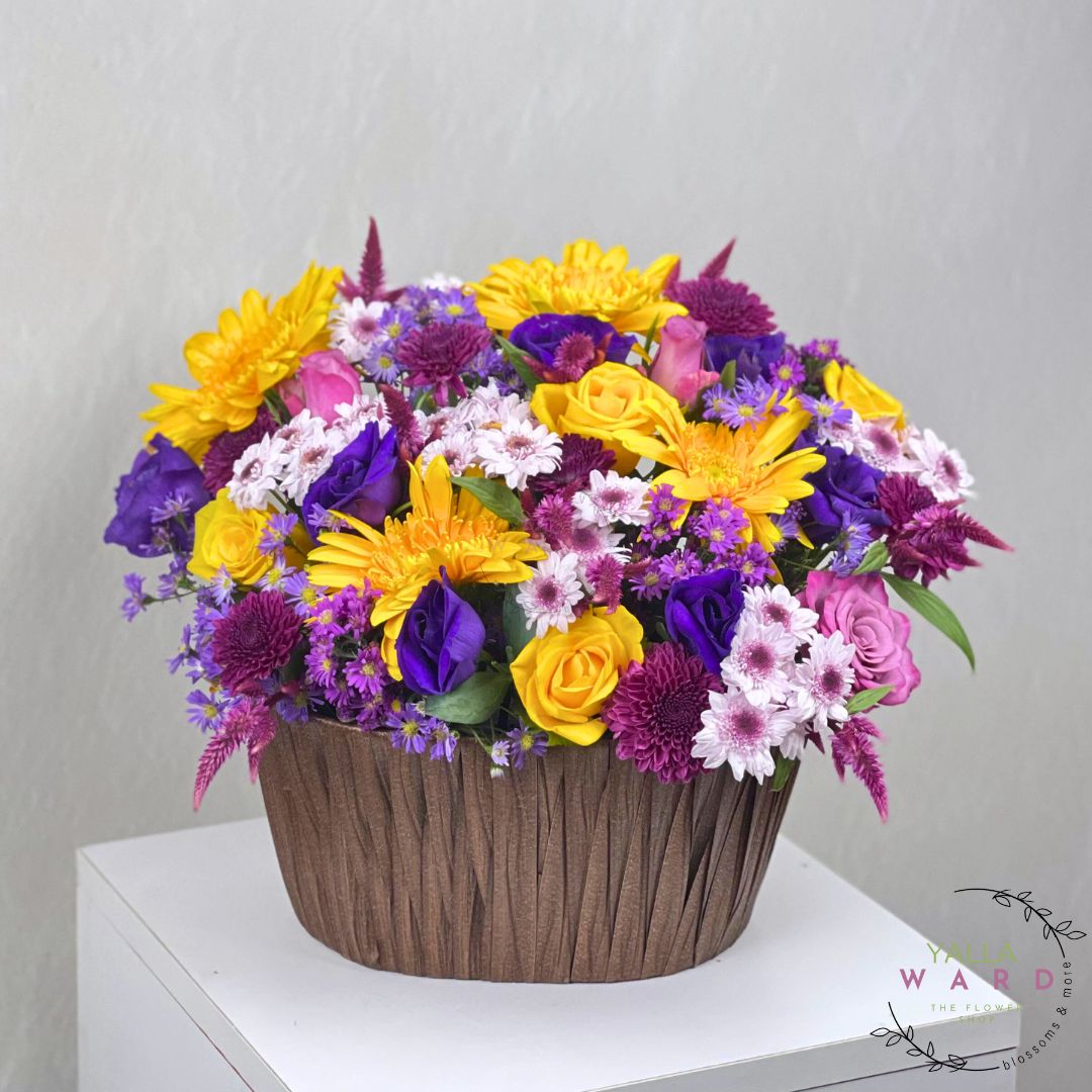 Colorful flower arrangement in a woven basket on a white surface with a gray background