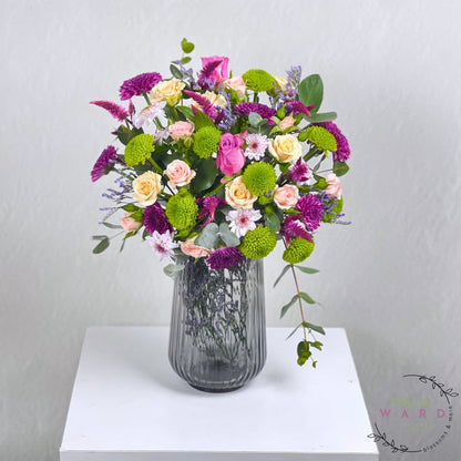 colorful flowers in a gray vase on a white surface with a light gray background.