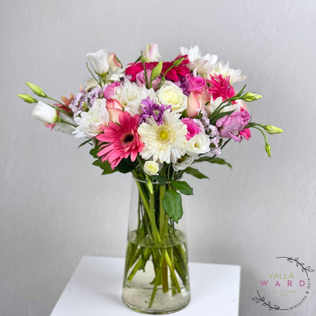 flowers in a clear vase on a white surface with a gray background