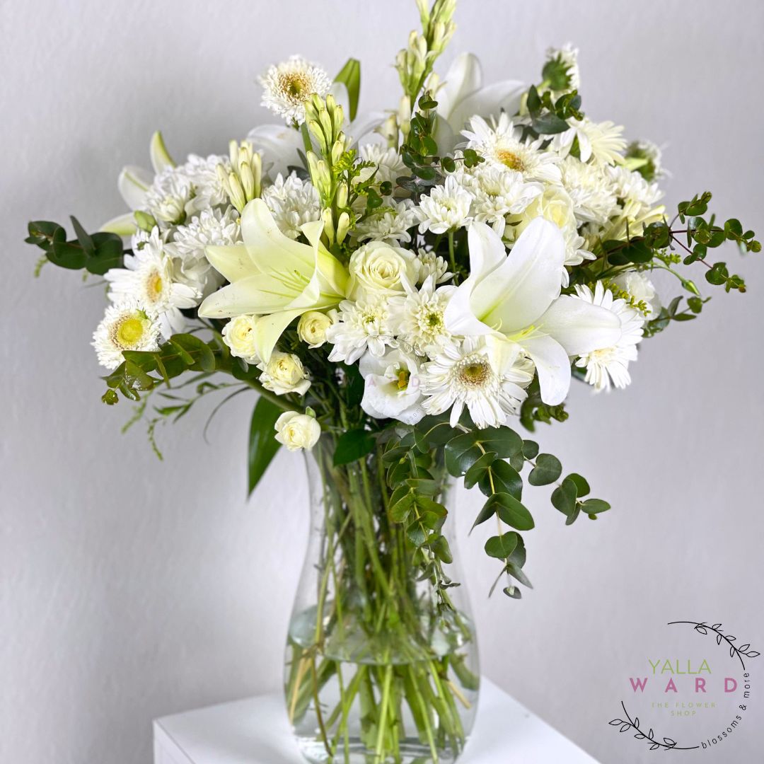 white and green flowers in a clear vase on a light gray background