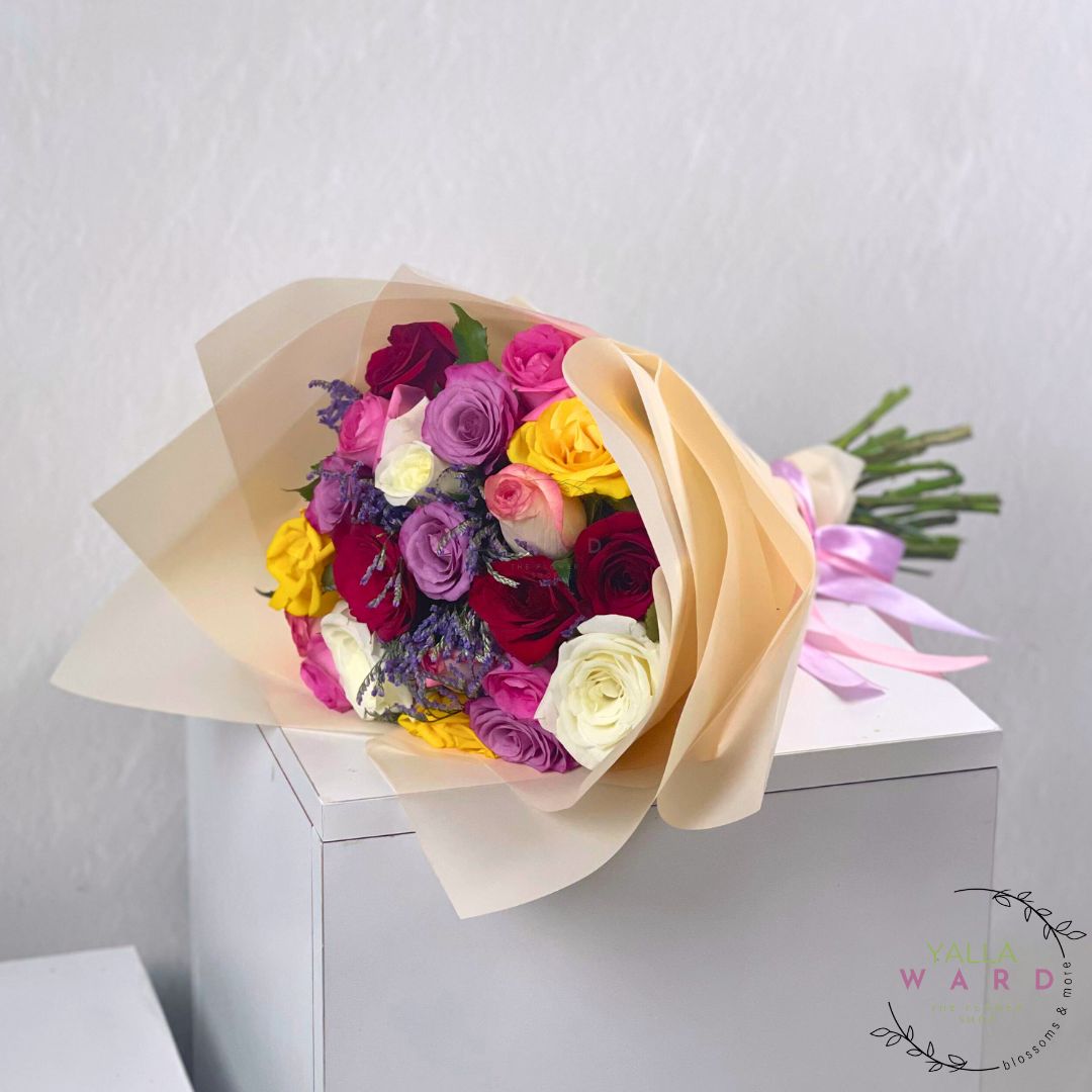 Colorful bouquet of flowers wrapped in beige paper on a white surface with a light gray background.