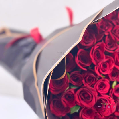 Bouquet of red roses wrapped in black paper with 'Yalla Ward' branding.