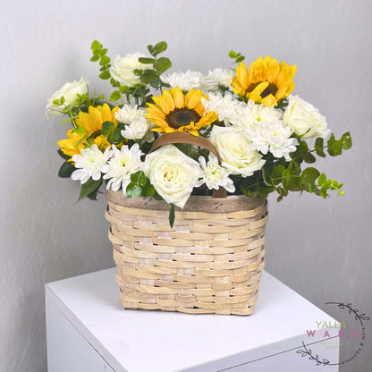Basket of flowers with sunflowers and white roses on a white surface against a gray background