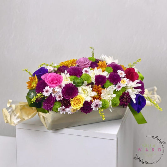 Colorful flower arrangement in a box on a white surface with a light gray background