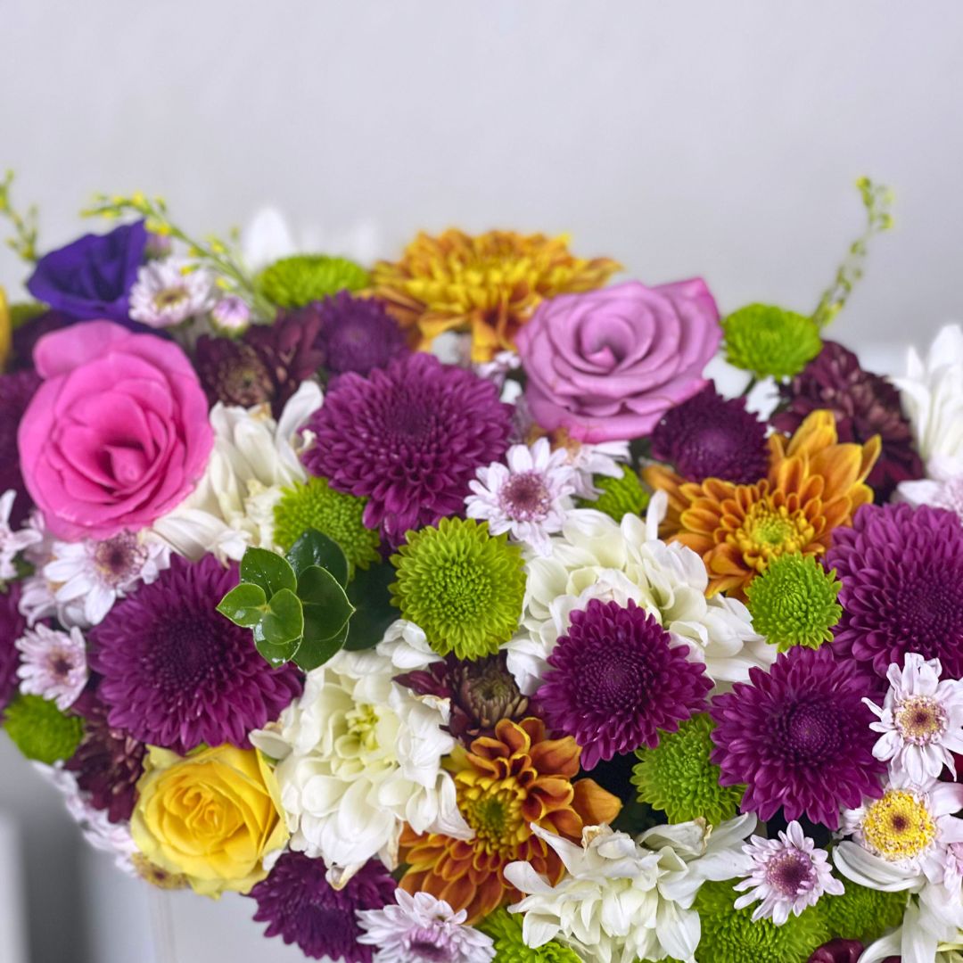 Colorful bouquet of flowers including roses, daisies, and chrysanthemums on a light gray background.
