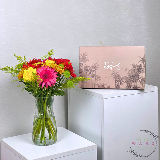 Colorful bouquet of flowers in a vase next to a dates  box on a white surface with a light gray background.