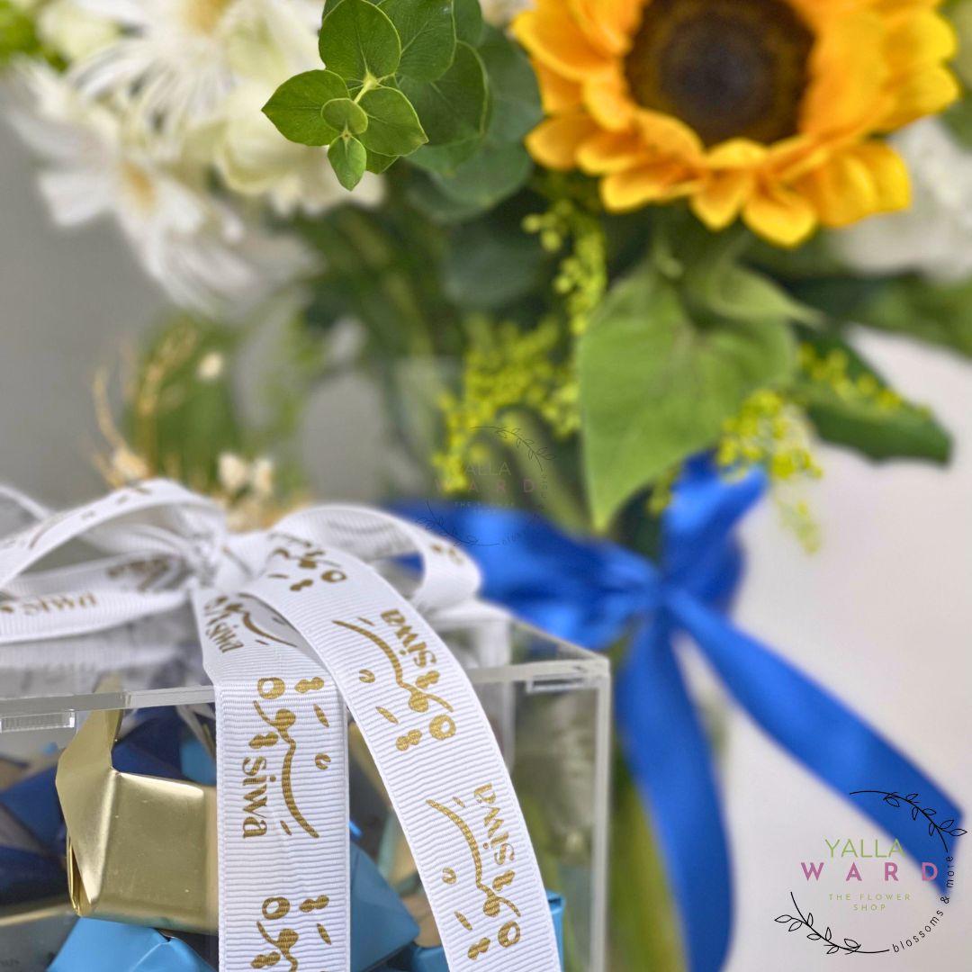 Bouquet of flowers with a blue ribbon and clear box, featuring a brand logo.