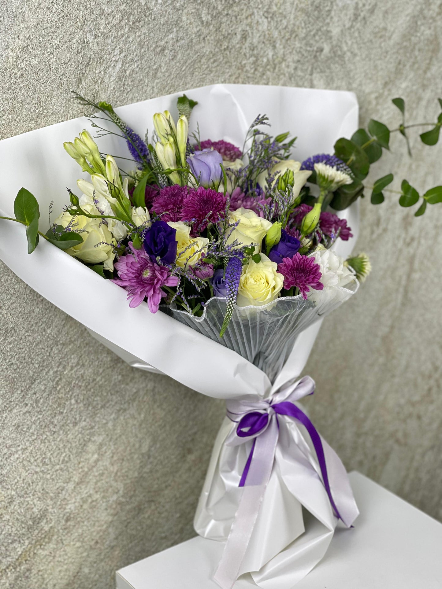 Bouquet of flowers wrapped in white paper with a purple ribbon on a neutral background