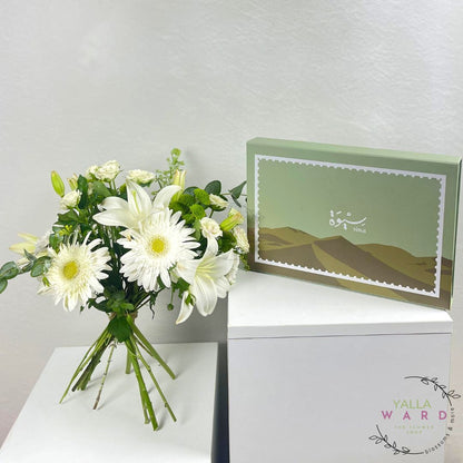 Bouquet of white flowers and a green box with a desert design on a white surface.