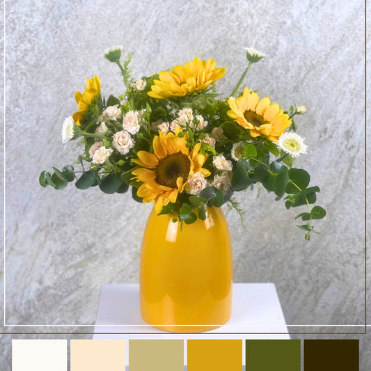 Yellow vase with sunflowers and greenery on a white surface against a light gray background