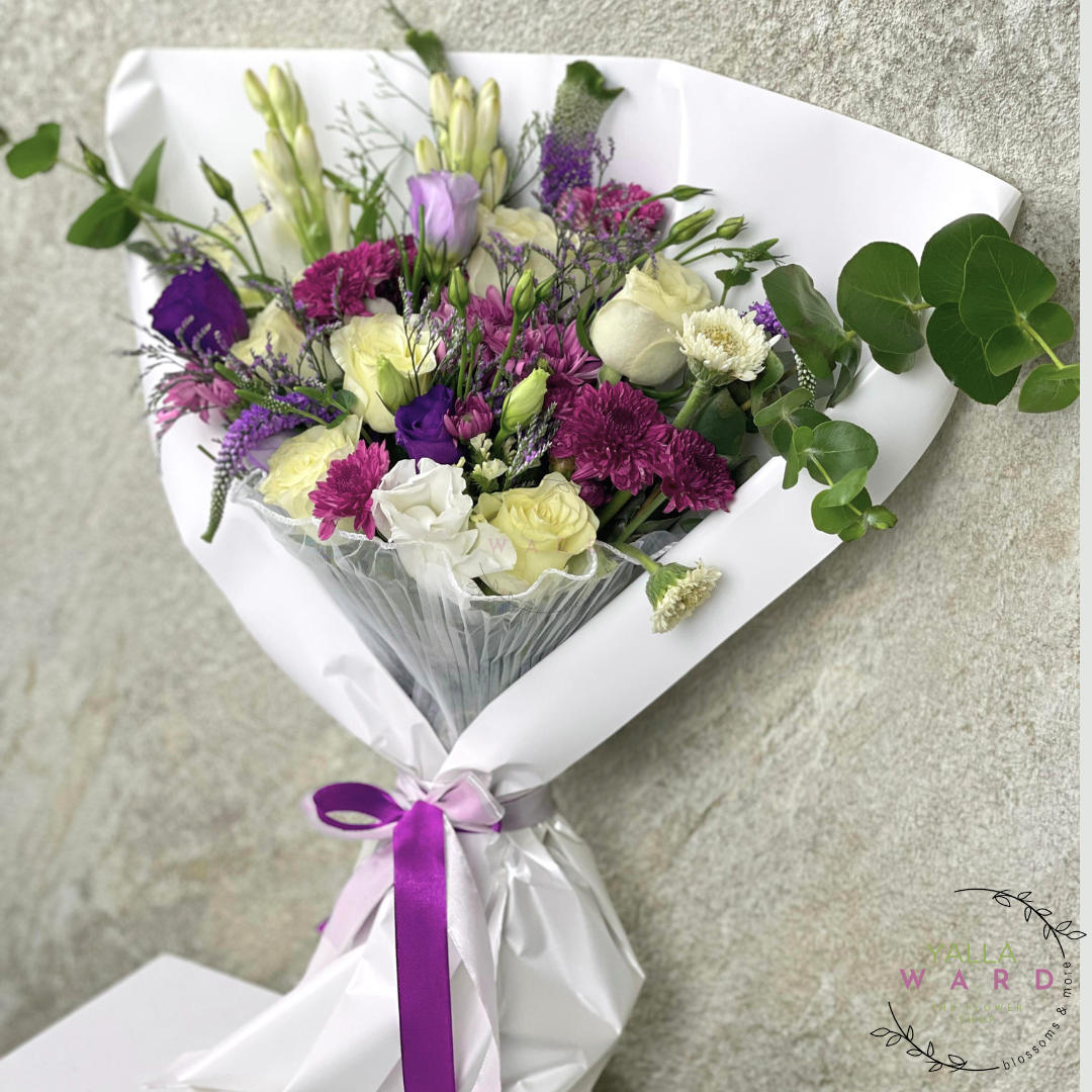 Bouquet of flowers wrapped in white paper with a purple ribbon on a gray surface.