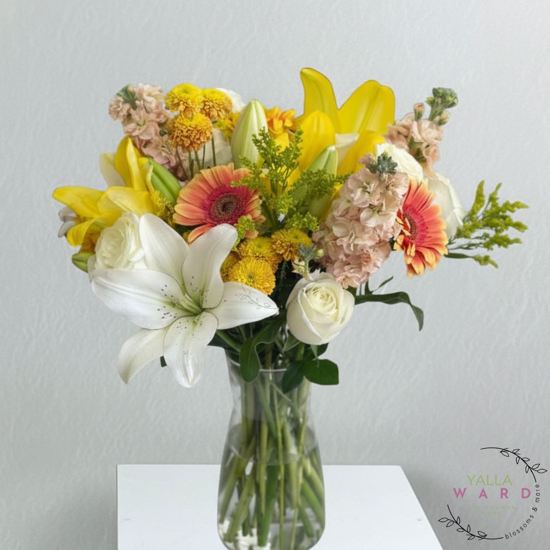 Bouquet of colorful flowers in a clear vase on a white surface with a light gray background.