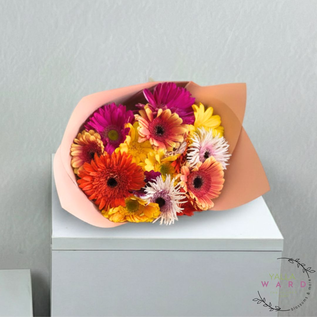 Bouquet of colorful flowers in a brown paper wrap on a white surface with a light gray background.