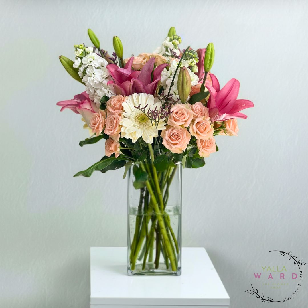 Bouquet of flowers in a clear vase on a white surface with a light gray background