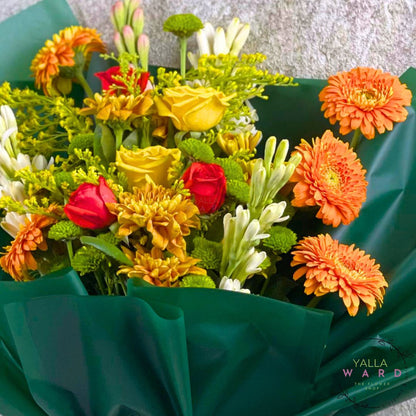 Bouquet of colorful flowers wrapped in green paper with 'Yalla Ward' branding.