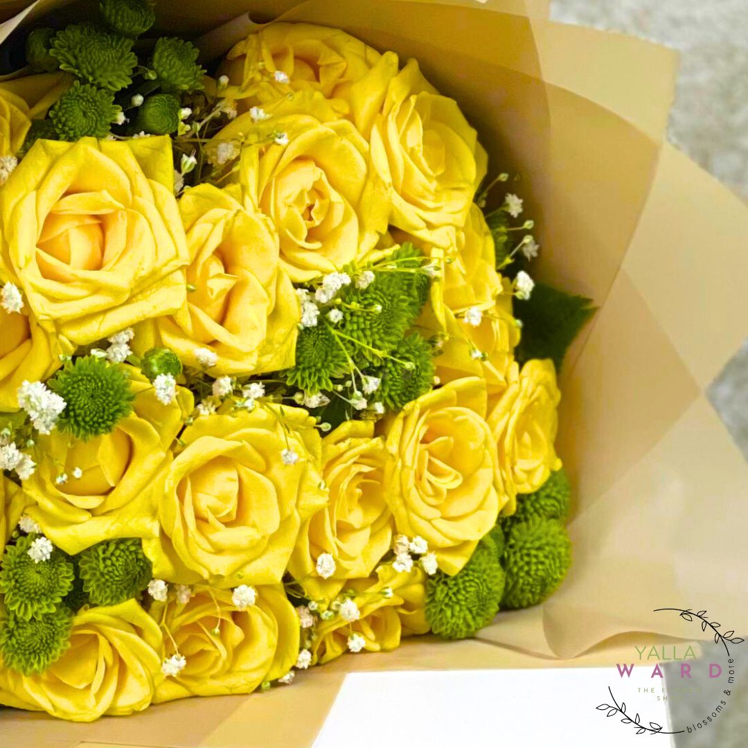 Bouquet of yellow roses with greenery and small white flowers, wrapped in brown paper, on a light background.