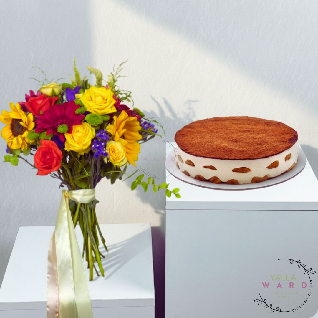 Bouquet of colorful flowers in a vase next to a cake on a white surface.